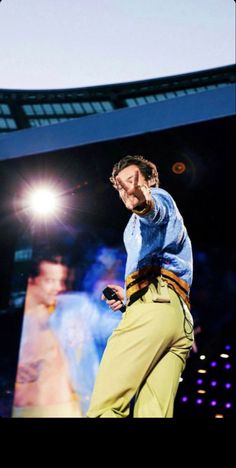 a man in blue shirt and khaki pants on stage with cell phone to his ear