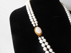 "A vintage white necklace. This is a beautiful necklace of summer white beads. The white bead necklace is a double strand of uniform size white beads, It is hand tied between each bead to prevent spillage. The necklace has a tab insert closure. This closure has a white cabochon in a goldtone setting. A beautiful summer necklace. MATERIAL: Beads CONDITION: Good SIZE: 28\" in length COLOR: White" Vintage Double Strand White Jewelry, Vintage White Double Strand Jewelry, White Oval Beads Single Strand Pearl Necklace, Classic White Beaded Pearl Necklace, Classic White Beaded Necklaces, White Single Strand Pearl Necklace With Oval Beads, Classic White Beaded Necklace, Vintage White Double Strand Pearl Necklace, White Double Strand Pearl Beaded Necklace