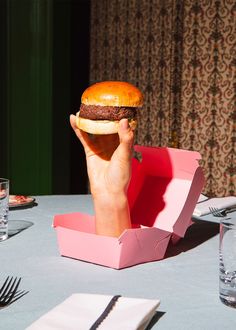 a person holding up a large hamburger in front of their face at a dinner table