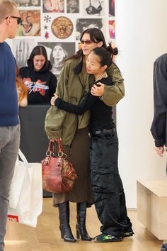 two women hug each other while standing in front of a wall with pictures on it