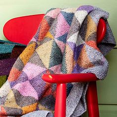 a chair with a blanket on top of it next to a red chair and green wall