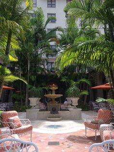 an outdoor fountain surrounded by chairs and palm trees