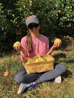 a woman sitting on the ground holding an apple basket