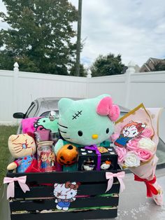 a hello kitty box filled with lots of stuffed animals and candy in front of a white fence