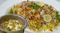 a white plate topped with lots of food next to a metal cup filled with rice