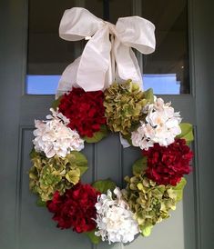 a wreath with red and white flowers hanging from the front door, decorated with a bow