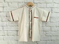 Boy's Traditional Handmade Mexican Guayabera Shirt - Beige - Off White Handmade in Chiapas, Mexico The embroidery pattern & embroidery colors will vary due to the handmade nature of the shirt. If you have any questions or requests please send us a message. Size 2 Measurements (approximate): Length: 12.5 - 13.5 inches Armpit to armpit: 10 - 10.5 inches Size 4 Measurements (approximate): Length: 13.5 - 14 inches Armpit to armpit: 11.5 - 12.5 inches Size 6 Measurements (approximate): Length: 15 - 1 Traditional Cotton Top With Stand Collar, Traditional Beige Short Sleeve Tops, White Cotton Tops With Traditional Patterns, White Cotton Top With Traditional Patterns, Traditional Cotton Shirt With Motif, Traditional Short Sleeve Cotton Kurta, Traditional Short Sleeve Summer Kurta, Traditional Embroidered Short Sleeve Sets, Summer Cotton Kurta With Woven Motifs