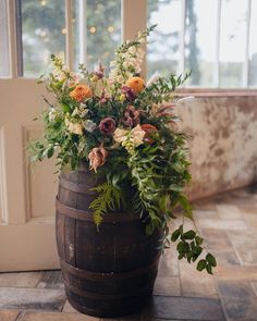 a wooden barrel filled with flowers on top of a tiled floor next to a window