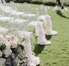 rows of clear acrylic chairs with white flowers and greenery on the grass