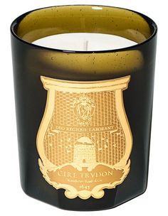 a black candle with gold trim and a crest on it's side, sitting in front of a white background