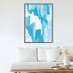 a living room with a white couch and blue art work on the wall above it