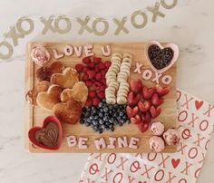 a wooden cutting board topped with different types of food next to valentine's day treats