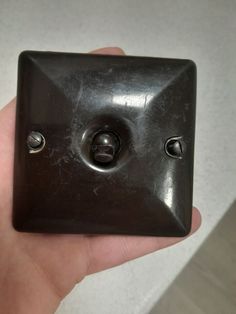 a hand holding a black square shaped object with two screws on the front and one hole in the middle