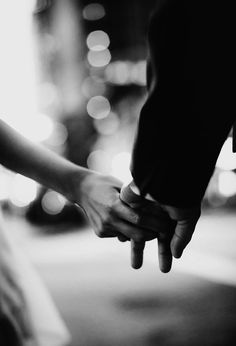 black and white photograph of two people holding each other's hands with blurry lights in the background