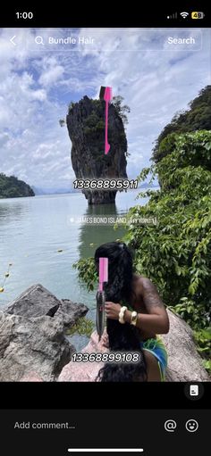 a woman sitting on top of a rock next to the ocean holding a pink object