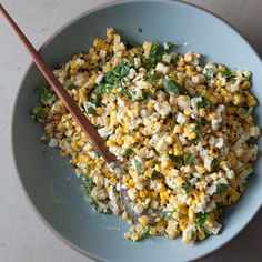 a bowl filled with corn and vegetables next to a wooden spoon on a white table