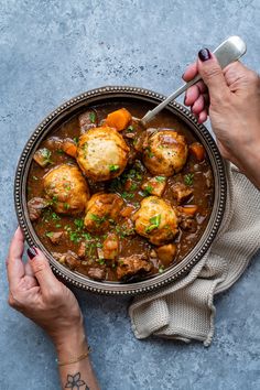 two hands holding a bowl of stew with potatoes and meat