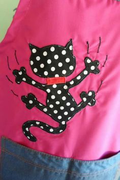 a pink apron with black and white polka dot cat on it's front pocket