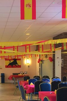 a banquet hall with tables and chairs covered in red, yellow and blue tablecloths