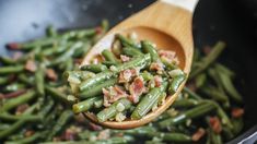 a wooden spoon filled with green beans and bacon