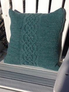 a green knitted pillow sitting on top of a white bench next to a chair