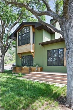 a green house with stairs leading up to the second story and trees in front of it