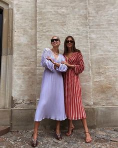 two women standing next to each other in front of a stone building with doors and windows