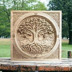 an intricate carved wooden plaque with a tree in the center on a picnic table outside