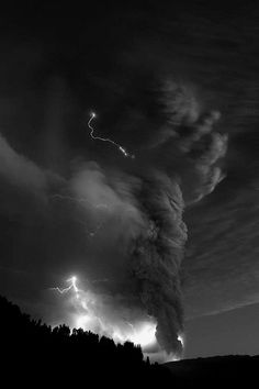 a black and white photo of a cloud with lightning in the sky over trees on a hill