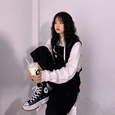 a woman sitting on top of a white toilet holding a drink and looking at the camera