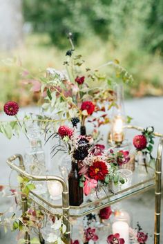 a table topped with vases filled with flowers and greenery next to candles on top of a metal stand