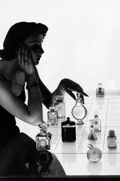 a woman is sitting at a table with many perfume bottles on it and holding her hand to her face