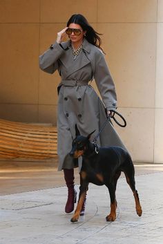 a woman in a trench coat walking her dog