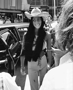 a woman wearing a cowboy hat walking down the street with other people in the background