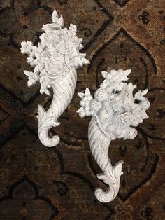 two white vases sitting on top of a carpet covered in floral designs next to each other