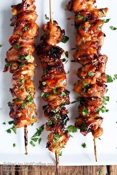 three skewers of chicken on a white plate