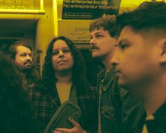 a group of people standing next to each other on a subway train, looking at something in the distance