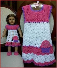 a doll is next to a crocheted baby dress on a chair with a pink bow