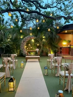 an outdoor ceremony setup with white linens and gold chairs, lit up by lanterns