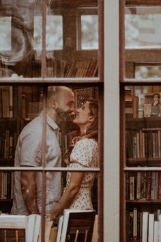 a man and woman kissing in front of bookshelves