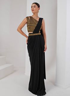 Introducing the stunning Black Pre-Draped Saree Set, crafted from luxurious lycra and crepe. This elegant black saree features beautifully pleated pallu detailing that creates a sophisticated drape, effortlessly merging modern convenience with the timeless grace of traditional attire. Paired with a chic sleeveless blouse, showcasing a contemporary one-shoulder neckline and adorned with intricate nalki embellishments that add a subtle shimmer. A hand-embellished belt cinches the waist, providing a stylish accent that perfectly ties the look together. Ideal for cocktails or high-end parties, this saree ensures you make a statement with its unique fusion of tradition and trend. Composition : Blouse - Crepe blend & Saree - Lycra Care: Dry Clean Only and Vacuum Storage This product can be custo Festive Fitted Pre-draped Saree For Gala, Elegant Black Pre-draped Saree, Elegant Black Pre-draped Saree For Evening, Black Bollywood Style Pre-draped Saree, Black Bollywood Pre-draped Saree, Festive Black Draped Saree, Black Pre-draped Saree For Party, Black Georgette Draped Saree, Black Draped Georgette Saree