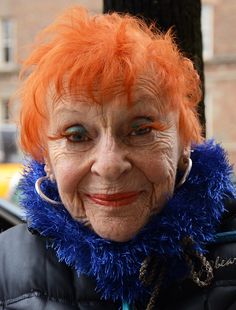 an older woman with bright orange hair and blue fur around her neck