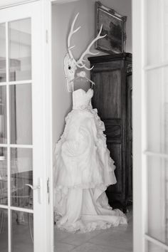 a wedding dress hanging on the wall in front of an open door with deer antlers