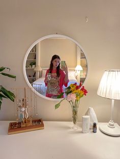 a woman standing in front of a mirror next to a vase with flowers on it