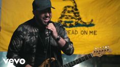 a man singing into a microphone and holding a guitar in front of an american flag