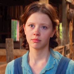 a young woman with blue eyes stares into the camera while standing in front of a barn