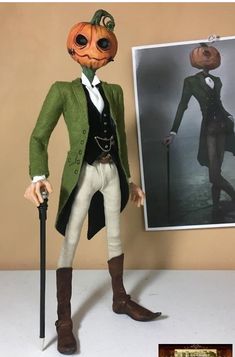 a doll is dressed in an old fashion outfit and holding a cane, standing next to a photograph