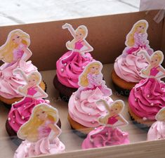 cupcakes decorated with pink frosting and barbie doll figurines in a box