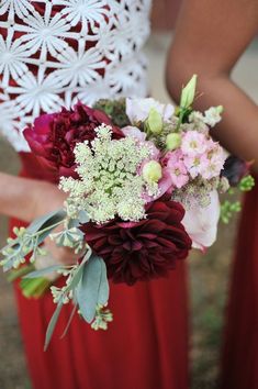 two bridesmaids in red dresses hold their bouquets with white and pink flowers