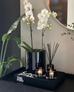 two vases with flowers and candles on a table in front of a round mirror